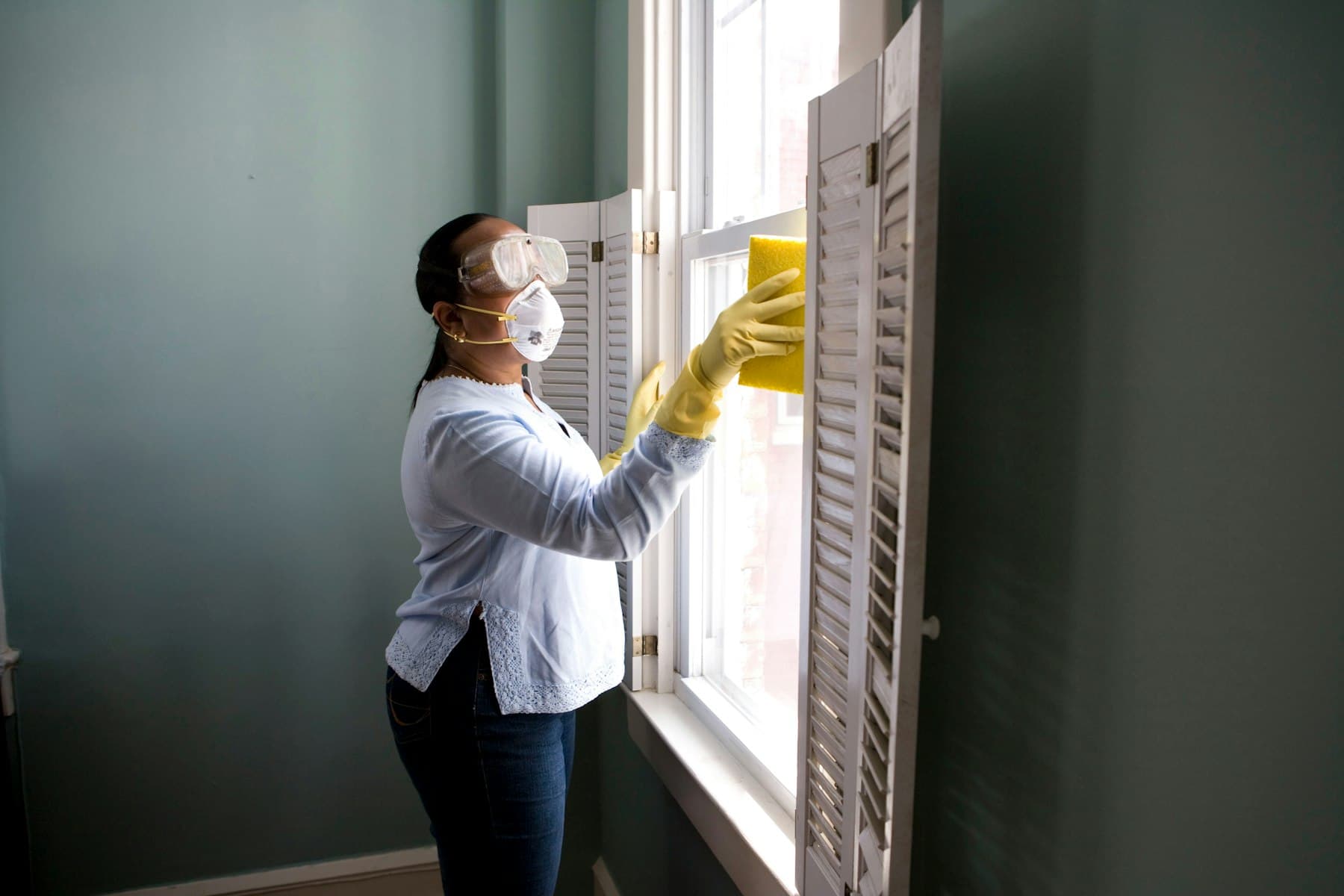 A cleaner wearing gloves wiping down a window frame