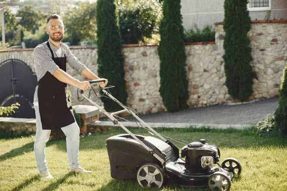 A groundsman mowing a lawn beside a hedge